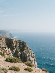 Breathtaking view of a rugged cliffside overlooking a calm, deep blue ocean under a clear, sunny sky.
