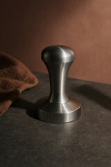 Close up image of a sleek, stainless steel coffee tamper, sitting on a dark countertop, suggesting preparation and quality