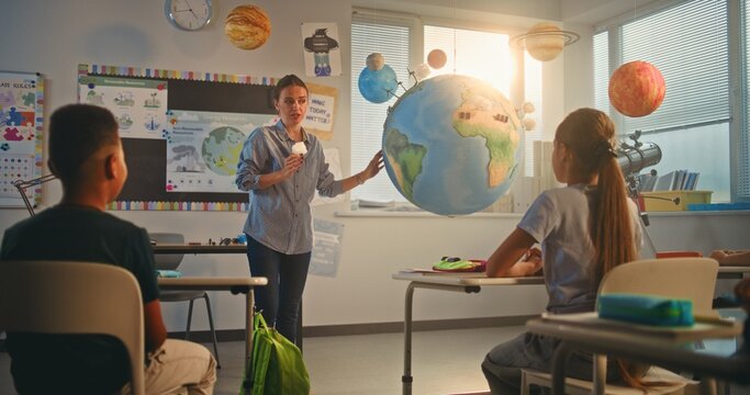 STEM Class on Renewable Energy: Female Teacher Explaining Energy Resources to Elementary School Students Using Model of Planet Earth. Diverse Kids Learning Science in Modern Classroom. Slow Motion.