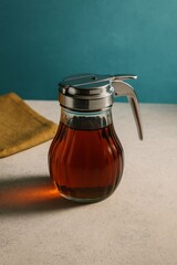 Maple syrup in a classic dispenser on a textured surface with blue background