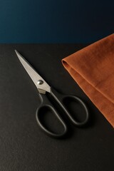 Sharp scissors and folded fabric on a dark surface 