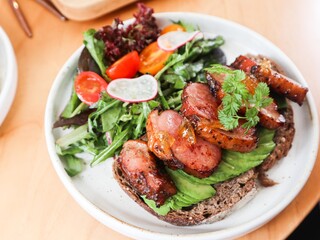 close up of sourdough toast with avocado slice and duck breast in yuzu sauce. Lecttuce and cherry tomato on the side on a white plate 