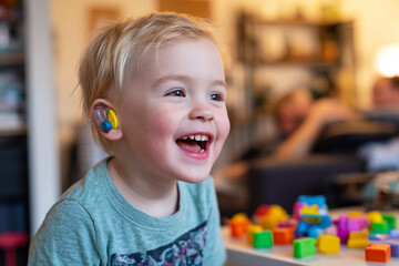 Smiling toddler wears hearing aid in indoor setting. Represents accessibility, childhood, technology. Great for marketing, design, editorial purposes.