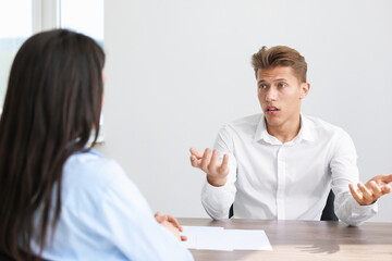 Young man complaining to woman at wooden table indoors