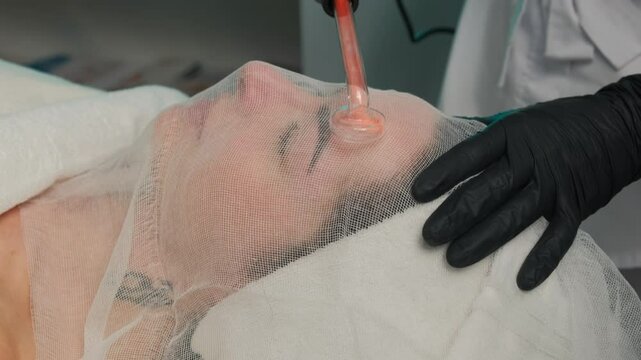 Woman receiving high-frequency facial treatment with Darsonval device in a beauty salon. Skincare and rejuvenation concept.
