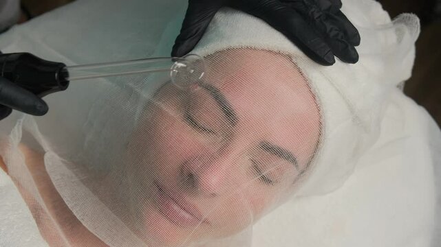 Woman receiving high-frequency facial treatment with Darsonval device in a beauty salon. Skincare and rejuvenation concept.