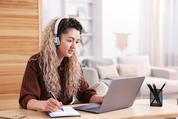 Woman in headphones working with laptop at desk in home office