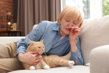 Senior woman suffering from allergy with her cat on sofa at home