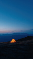 Glowing tent under blue twilight sky on mountain ridge