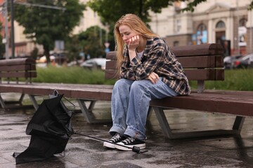 Frustrated woman sitting near broken umbrella on bench outdoors