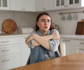 Worried woman suffering from paranoia at table in kitchen