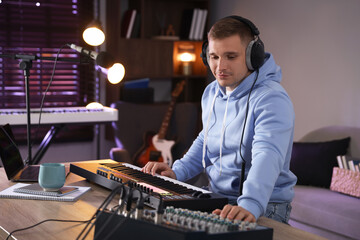 Man in headphones working with MIDI keyboard and dj mixer at table in home studio