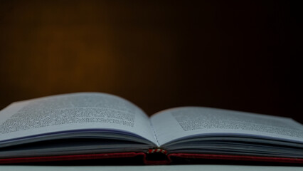 Open book with blurred text under warm light against black background, moody still life concept...