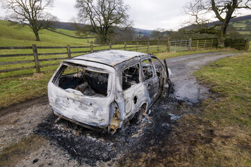 Burnt-out car sits abandoned on a muddy track in a rural countryside