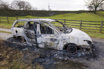 Burnt-out car sits abandoned on a muddy track in a rural countryside