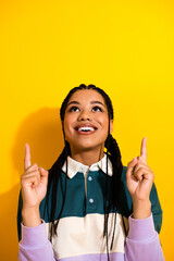 Cheerful young woman in casual clothing making a pointing gesture with both hands on a vibrant...