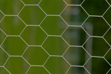 This closeup photo of a hexagonal wire mesh fence emphasizes its unique design against a soft green...