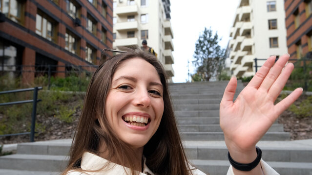 Close-up portrait of attractive young Caucasian girl smiling and looking at camera, taking selfie video. Cute woman broadcasting video with smartphone, waving at webcam - Powered by Adobe