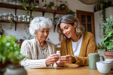 Woman helps senior with medication at home. Shows care, family, health. Useful for ads, web, design.