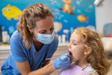 Dentist examines young girl's teeth in colorful office. Happy child receives dental care. Useful for marketing, advertising, websites, print.