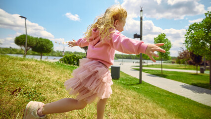 Side run glow. Joyful child runs in a park under a clear blue sky, exuding happiness and carefree...