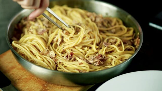 Mixing Italian Spaghetti Carbonara Pasta With Bacon In Frying Pan Using Culinary Tongs