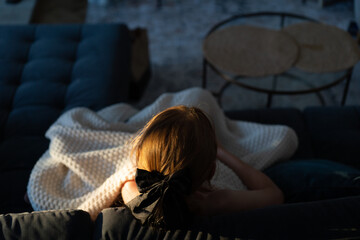 girl with a bow in her hair sitting on a sofa under the blanket. Aesthetic warm cozy picture