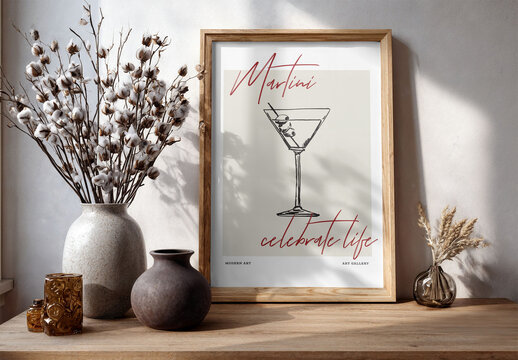 A wooden frame stands empty on a table beside decorative vases and cotton branches, creating a contemporary home decor setting. PSD template mockup