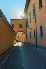  A charming, sun-drenched Italian alleyway features warm-toned buildings, an ancient archway, and...