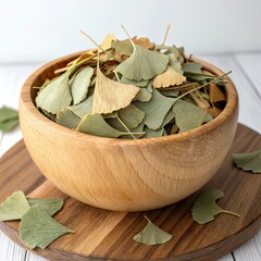 Fototapeta premium a wooden bowl filled with dried ginkgo biloba leaves placed on a wooden surface against a plain white background