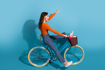 Young stylish woman riding a blue bicycle against a vibrant background expressing joy