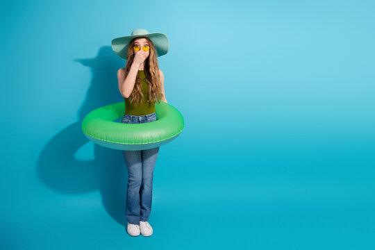 Cheerful young woman in summer outfit with green flotation ring posing against vibrant blue background in a relaxed mood - Powered by Adobe