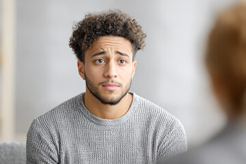 Obraz premium A young man with curly hair wearing a gray sweater looks concerned or unsure while facing someone whose back is to the camera.