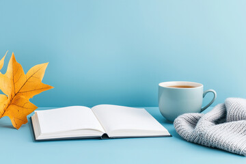 Naklejka premium Cozy home setup featuring open notebook, cup of tea, soft sweater, and vibrant autumn leaf, creating warm and inviting atmosphere for relaxation and creativity