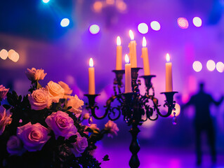 A close-up of a candelabra with lit white candles next to a bouquet of pink and white flowers, all set against a blurry purple background with bokeh lights.