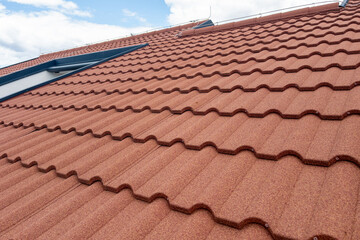 Textured red roof tiles on a residential building under a bright blue sky with clouds