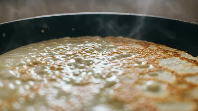 Cooking pancake batter in a large frying pan with steam rising  