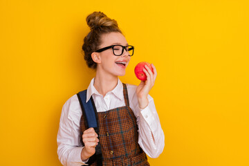 Smiling student in stylish uniform enjoying a red apple against a vibrant yellow background
