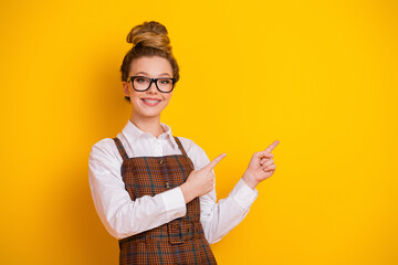 Cheerful student with stylish attire pointing on bright yellow backdrop illustrating youthful...