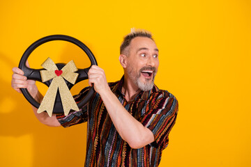 Happy man holding decorated gift steering wheel against a vibrant yellow background in a festive...