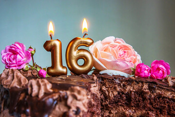 Sweet sixteen chocolate birthday cake decorated with golden glowing lit 16 candles and pink roses....