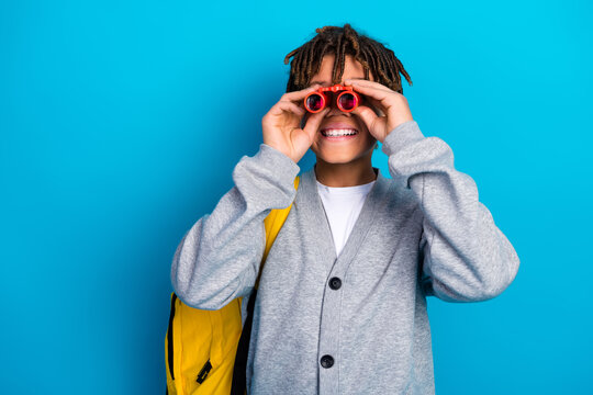 Happy schoolboy in casual uniform with a backpack using binoculars on a blue background, emphasizing joy and exploration