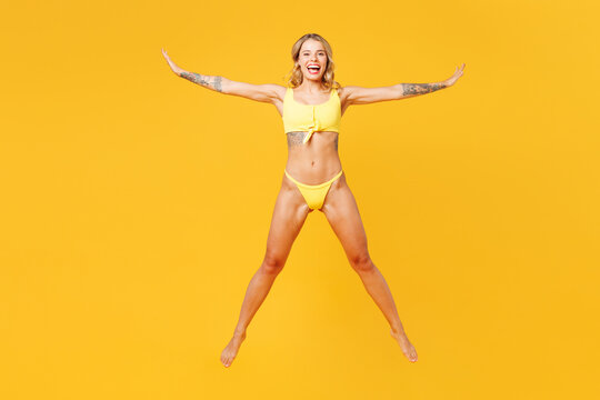 Full body young carefree beautiful sexy woman she wear bikini swimsuit rest near hotel pool jump high with outstretched hands isolated on plain yellow background. Summer vacation sea sun tan concept.