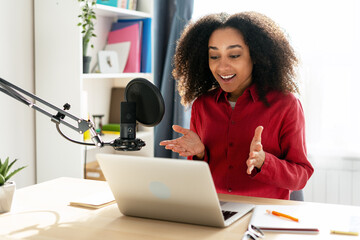 Young African American woman recording podcast from her home studio using microphone and laptop