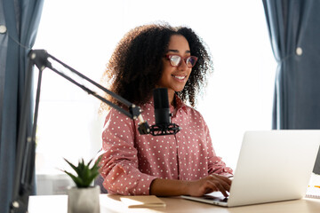 Smiling African American woman recording podcast using laptop and microphone at home