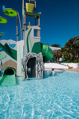 A child is playing in a pool with a slide. The pool is surrounded by trees and has a green slide