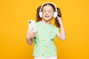 Little smiling fun kid child girl 8-9 years old wears green t-shirt listen to music in headphones...