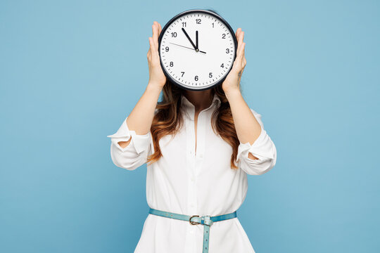 Young successful employee business woman corporate lawyer wear shirt classic formal clothes work in office hold in hand cover eye with clock isolated on pastel light blue background studio portrait.