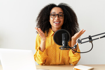Smiling African American woman wearing stylish eyeglasses recording podcast from her home studio