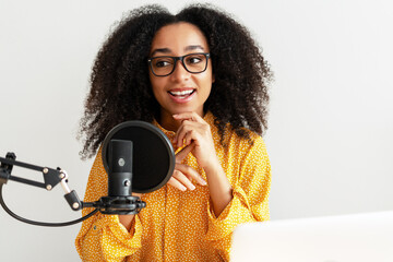 Young African American woman recording podcast using professional microphone and laptop